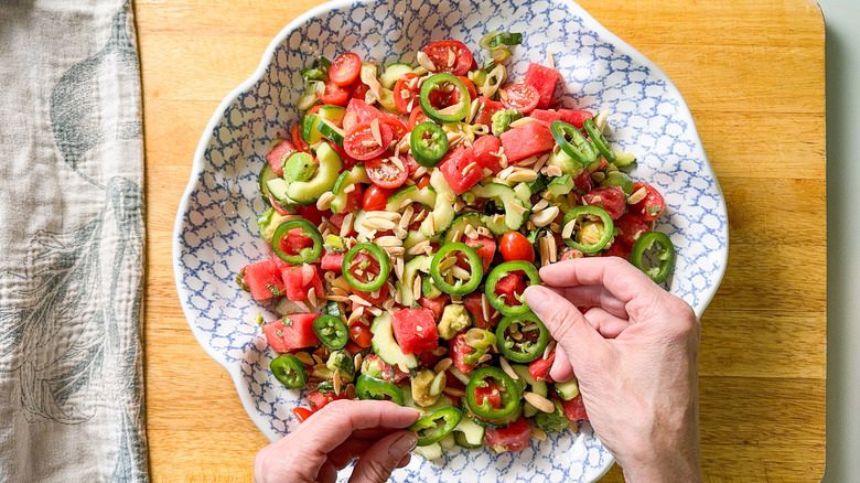 Garnishing deconstructed watermelon salad in serving bowl with jalape&ntilde;o slices and toasted almonds